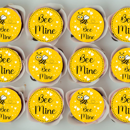 Cupcakes with 'Bee Mine' toppers arranged in rows on a gray background