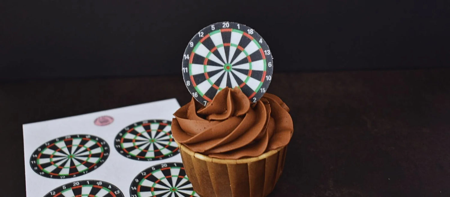 Edible Dartboard wafer cupcake topper, placed on top of a chocolate cupcake, with a sheet of wafer toppers placed to the side.