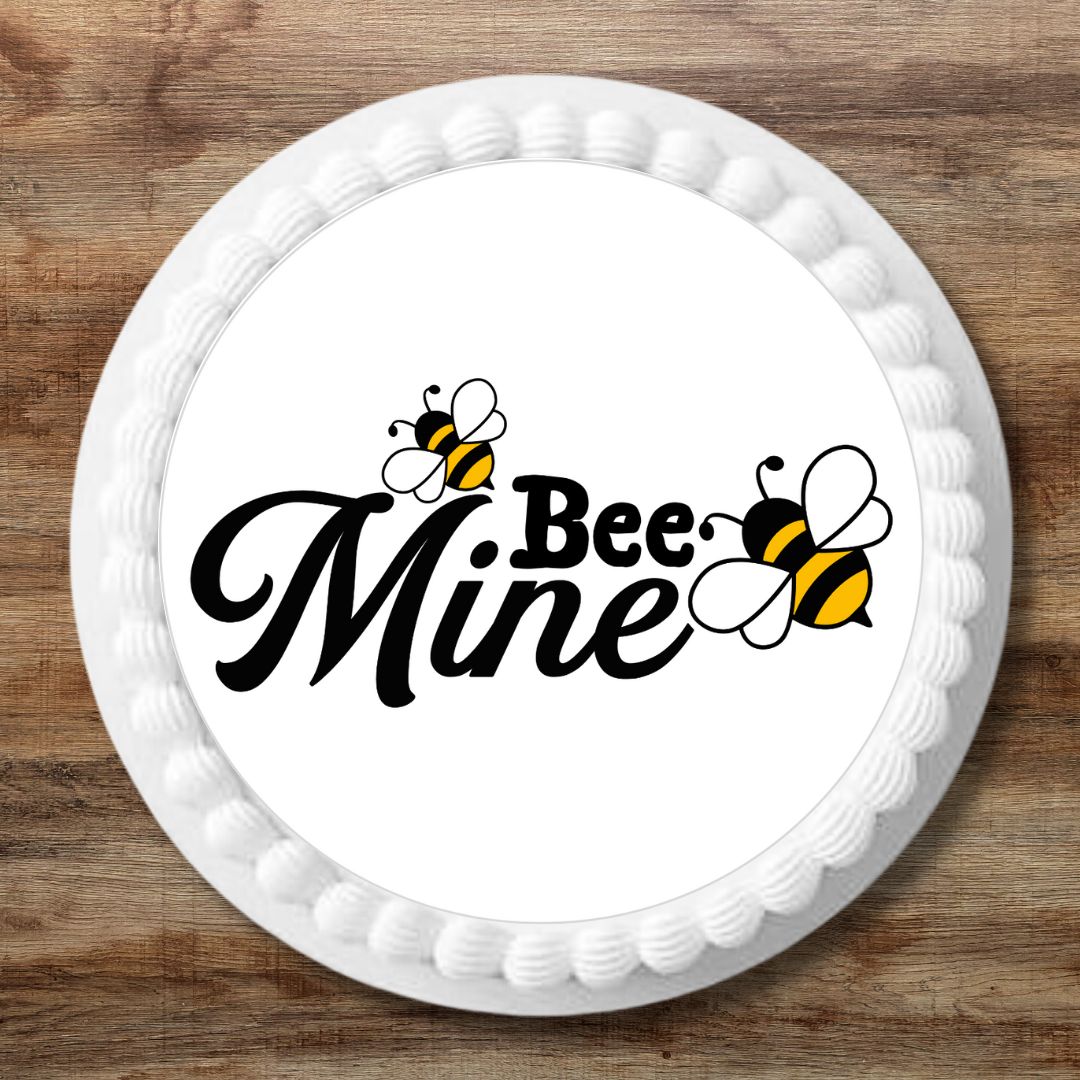 Round white cake with 'Bee Mine' text and bee graphics on a wooden surface