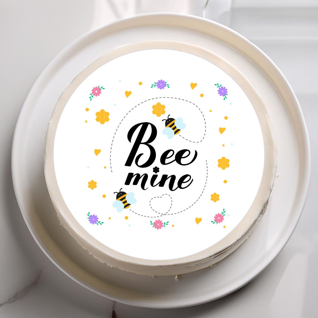 Round cake with 'Bee mine' text and bee illustrations on a white plate.