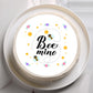 Round cake with 'Bee mine' text and bee illustrations on a white plate.
