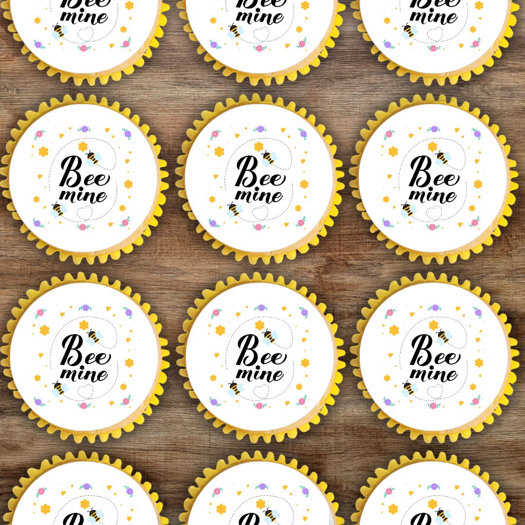 Cupcake liners with 'Bee mine' text on a wooden surface