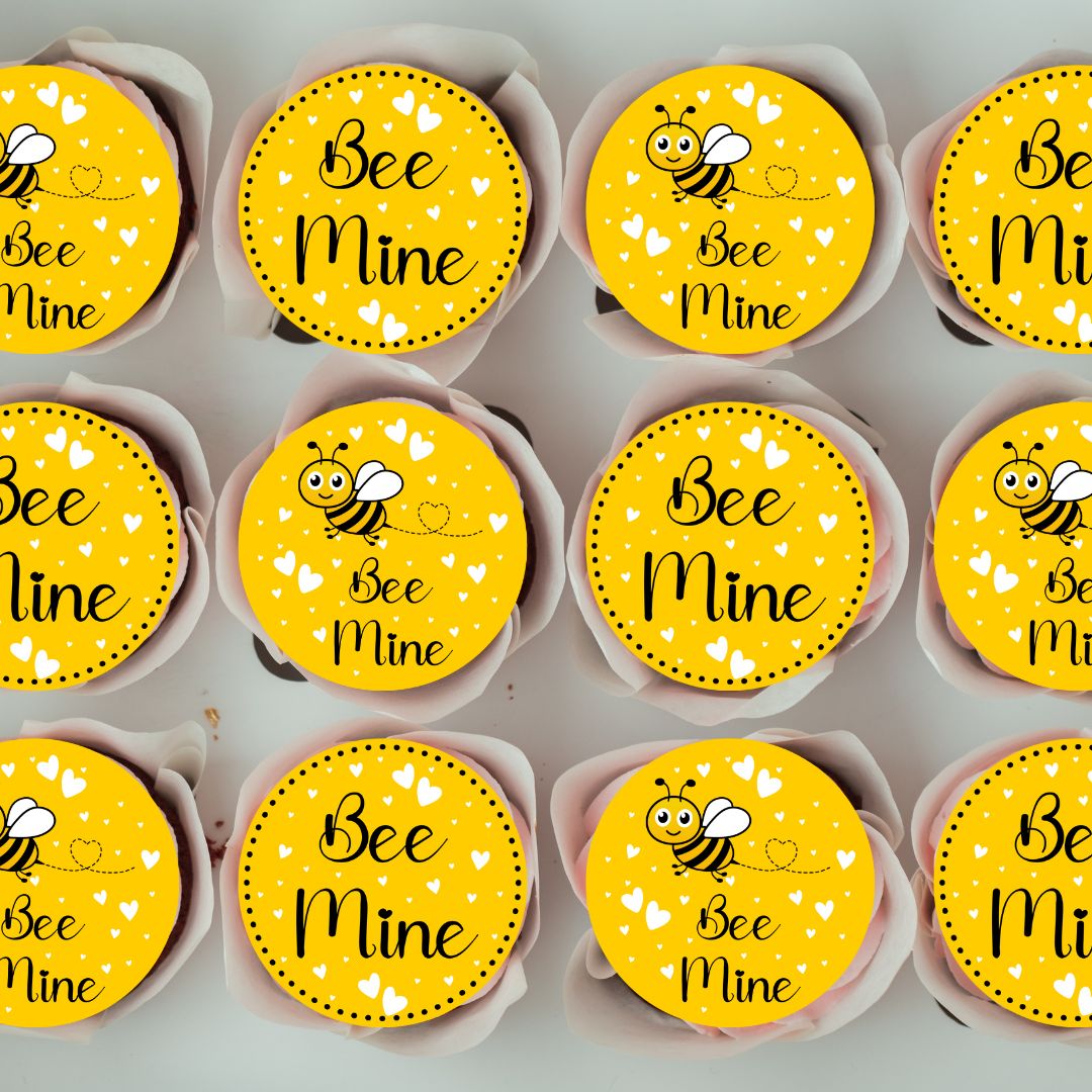 Cupcakes with 'Bee Mine' toppers arranged in rows on a gray background