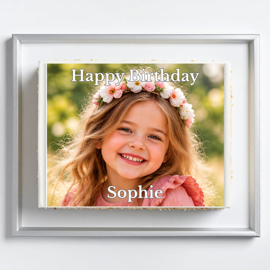 A framed personalized photo print featuring a smiling young girl with a flower crown and the text 'Happy Birthday Sophie' on a light gray background.