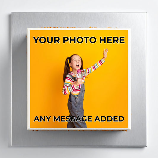 A square custom photo plaque or magnet with a brushed silver metallic border, featuring a bright yellow insert with placeholder text 'YOUR PHOTO HERE' and 'ANY MESSAGE ADDED' around a sample photo of a girl holding a microphone.
