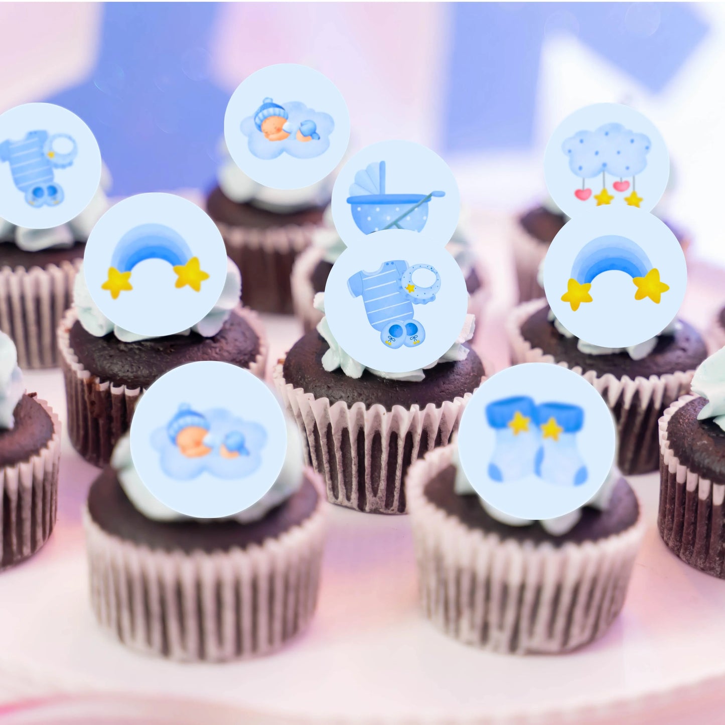 chcolate cupcakes decorated with blue illustrated cupcakes toppers with pictures of baby grows, blue rainbows and baby boys