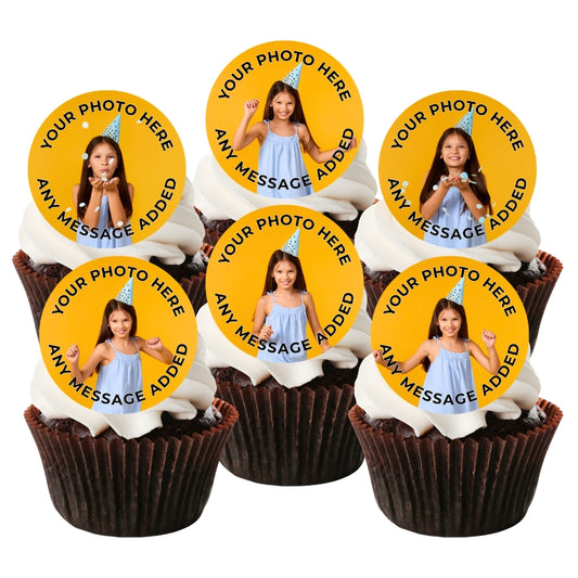 Six custom photo cupcake toppers displayed on top of white-frosted cupcakes. Each round yellow topper features a printed photo of a girl in a blue dress, with the text 'YOUR PHOTO HERE' and 'ANY MESSAGE ADDED' on a white background.
