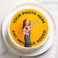 A round custom cake topper or printed cake insert displayed on a white cake stand. The insert features a bright yellow background with black placeholder text reading 'YOUR PHOTO HERE' and 'ANY MESSAGE ADDED', with a sample photo of a young girl in overalls and a striped shirt overlaid in the center.