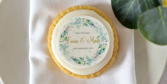 botanical wreath edible save the date toppers personalised with name and date placed on top of a cookie biscuit