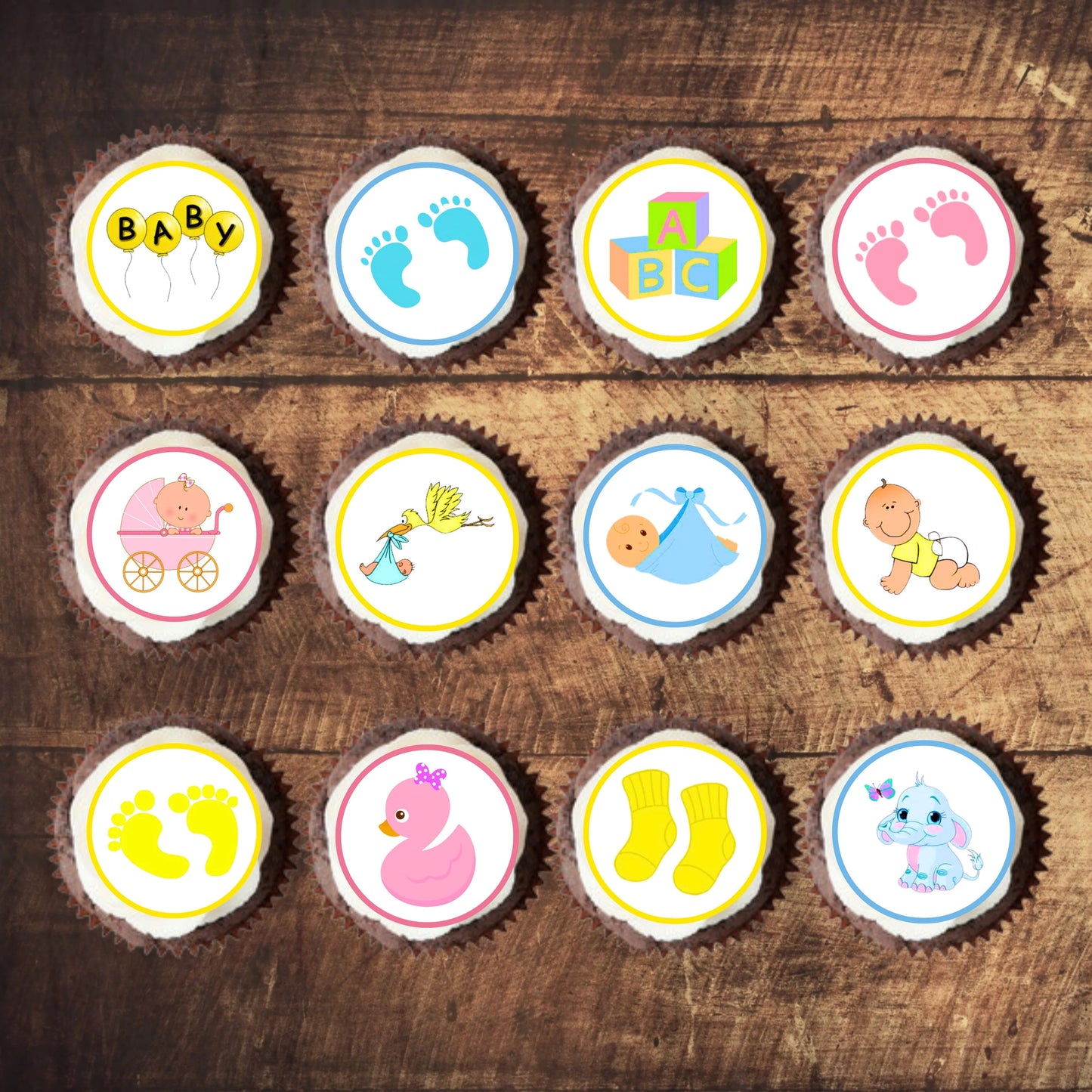 12 frosted cupcakes topped with pink, yellow and blue illustrated baby shower cupcake toppers