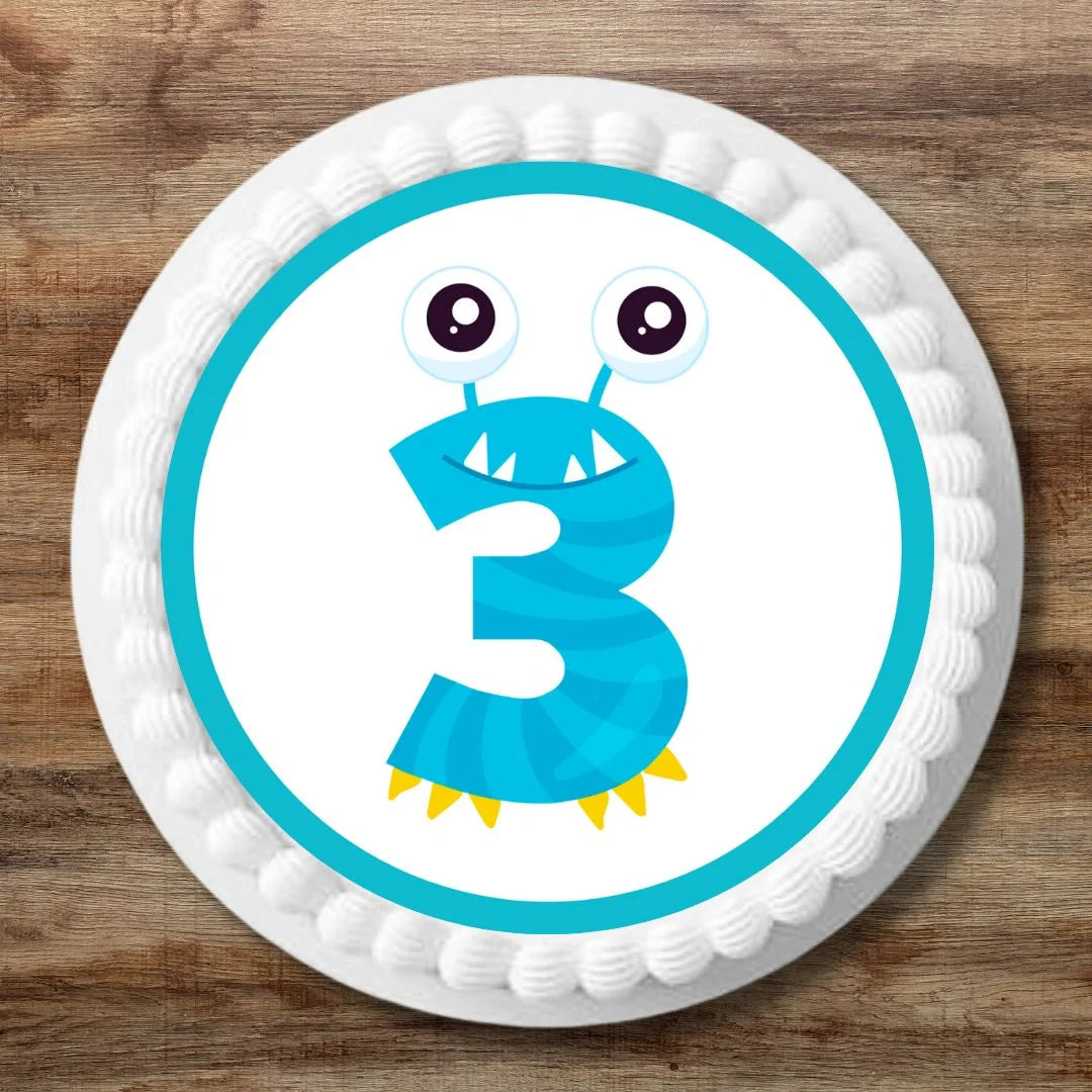 white iced birthday cake with a monster cake topper featuring a blue number 3 with monster eyes 